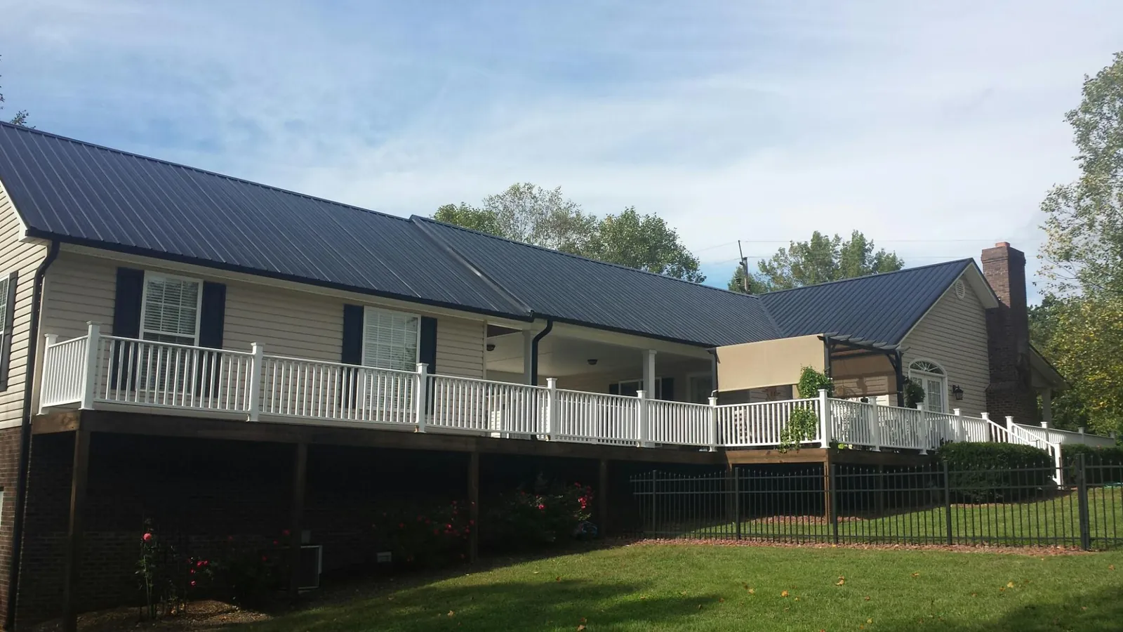 Black metal roof above a long white railed deck on a hillside home in Wheatland